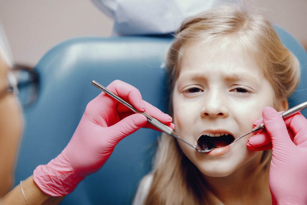 Medic pedodont care examinează un dinte de lapte afectat de carie